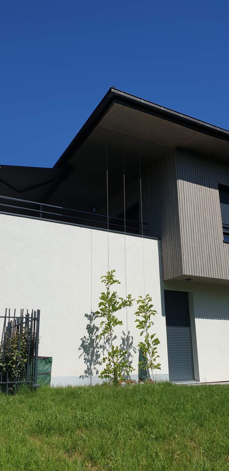Extérieur de maison moderne avec bardage en bois et balcon en verre sous un ciel bleu.