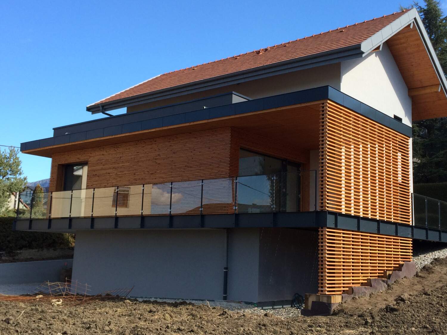Construction de maison en bois moderne avec bardage à lattes et grandes fenêtres.